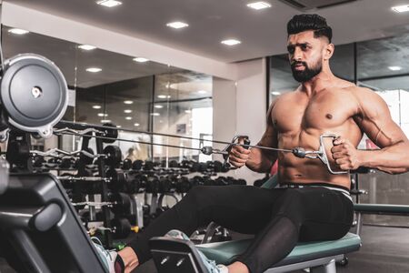 Athlete makes low cable pulley row seated in gym. Close back viewの写真素材