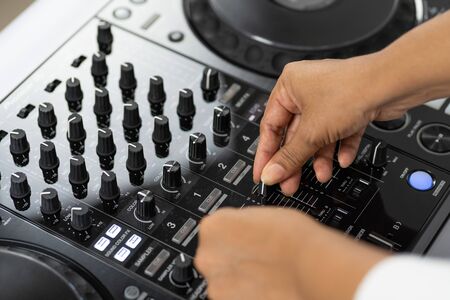 Hands of DJ mixing tracks on professional sound mixer.Fashionable rings on fingers of girl disc jockey playing music.Closeup,knobs and regulators in focus.Girl dj play music tracks at house partyの写真素材