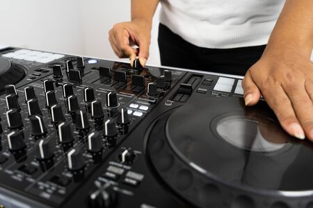 Hands of DJ mixing tracks on professional sound mixer.Fashionable rings on fingers of girl disc jockey playing music.Closeup,knobs and regulators in focus.Girl dj play music tracks at house partyの写真素材