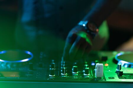club dj plays music on stage in nightclub.Hand of disc jockey adjusting sound track volume...