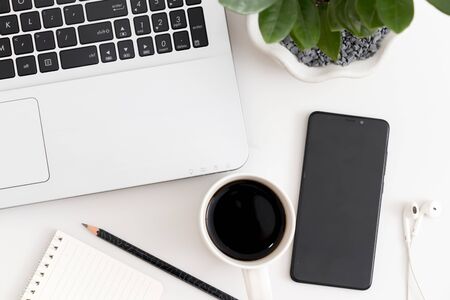 White office desk with laptop, coffee, mobile phone, notebook with pen. Top view with copy space, flat layの写真素材
