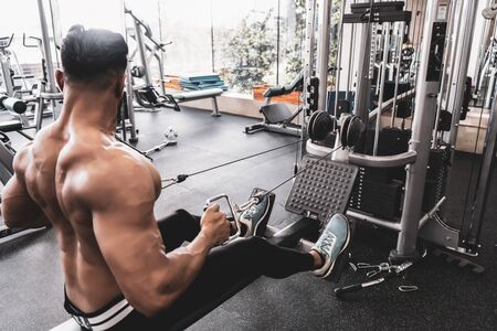 Athlete makes low cable pulley row seated in gym. Close back viewの写真素材