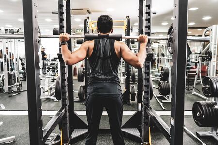 Man at the gym. Execute exercise squatting with weight, in gymの写真素材