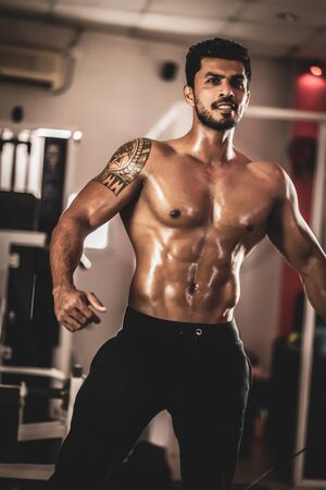 Muscular bodybuilder guy standing on gym and posing abdominal muscle
