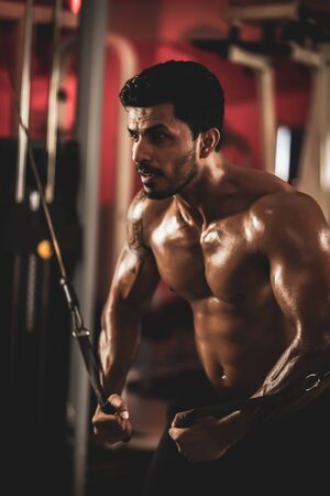 Muscular bodybuilder at cable crossovers fitness men pumping up muscles