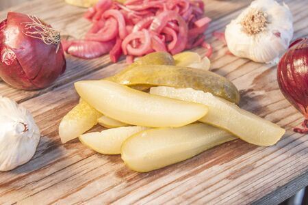 Pickled green cucumber, in front of red onions and garlicの写真素材