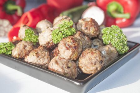 A black plate full of meatballs, in front of vegetableの写真素材