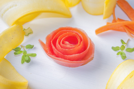 Red tomato flower, between yellow zucchini, carrot and herbsの写真素材