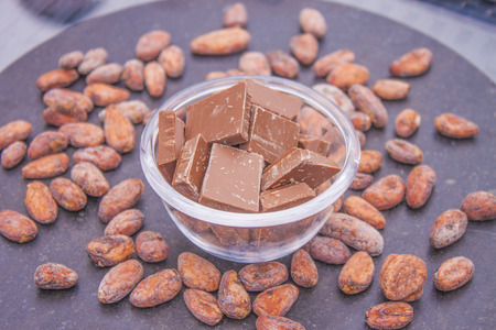 A lot of brown chocolate, in a glass bowl. Near cocoa beansの写真素材