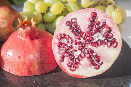 Two halves of a pomegranate, in front of apples and grapesの写真素材