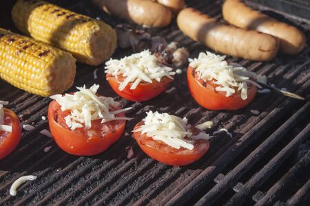 Red grilled tomatoes, on a barbeque, in front of sausage and cornの写真素材