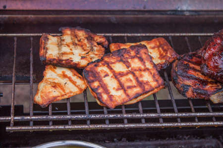 Slices of grilled halloumi, near meat, on a barbequeの写真素材