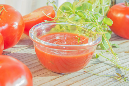 A glass bowl full of sweet pizza sauce, in middle of herbs and tomatoesの写真素材