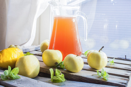 A can full of apple juice, near apples, mint, lemon and lime