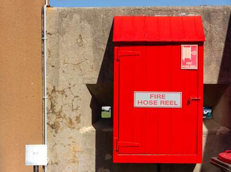 Red fire hose reel, mounted on old concrete wall background