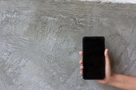 Asian woman hand hold moblie phone on grey cement backgroundの写真素材