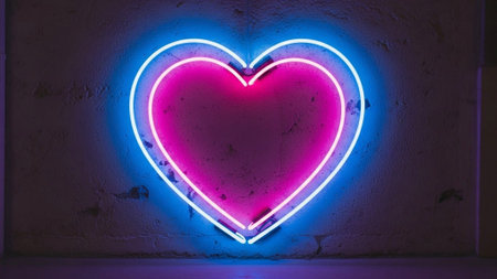 A neon heart shape with a bright pink interior and blue-white outline glows softly against a dark textured wall creating a warm ambient effect with visible light diffusion and subtle shadowsの素材