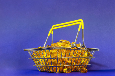Big capsules with a fish oil, a heap of golden jelly pills stacked in a grocery basket on a purple backgroundの写真素材