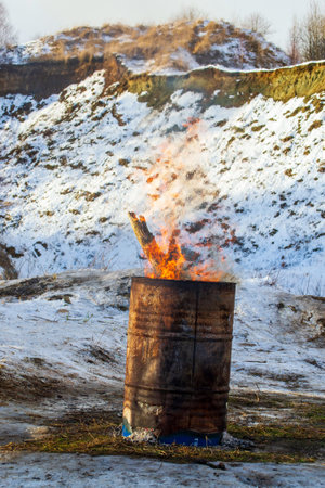 Flames rise from an old barrel in a snowy landscape during the winter seasonの写真素材