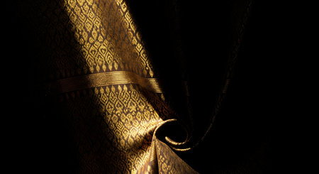 Close-up shot of a golden fabric with a detailed pattern, showcasing texture and folds, with a dark background.の素材