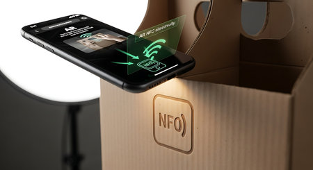 Close up view of a smartphone interacting with an NFC chip on a cardboard package. Concept of smart packaging, supply chain, and wireless data transfer.の素材