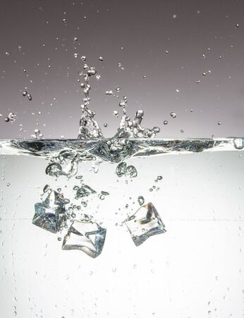 Ice cubes that just fell into the water and leave bubbles and a fountainの写真素材