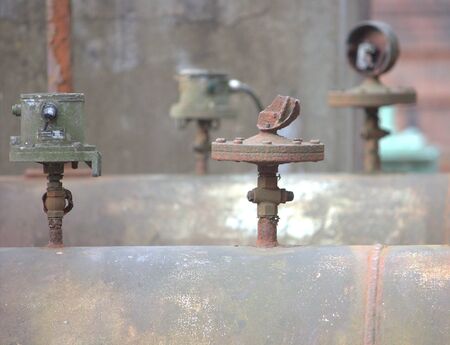 various valves on a large rusted pipeline in a disused factory