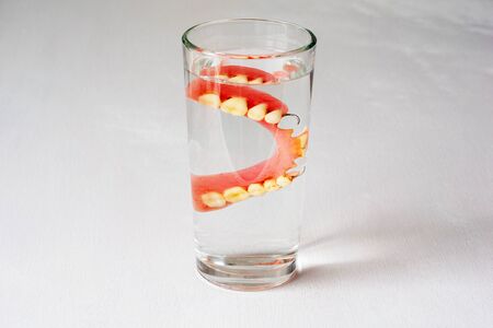 denture in a glass with water on a white background.