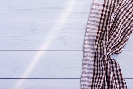 A white-brown checkered kitchen towel or cotton napkin lies on a gray wooden table. View from above....