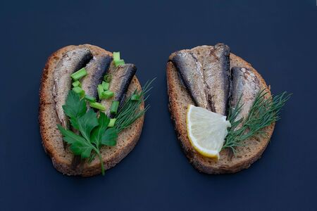 Sandwiches with sprats on bread with greens on a dark background. Sandwiches with sardines. Food photographyの写真素材