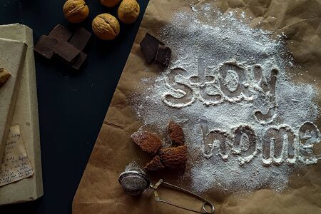 The inscription stay home made from white wheat flour. Scattered cookies, nuts, chocolate on a dark...