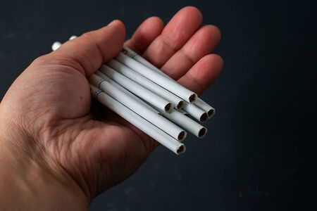 Hand holds white thin cigarette with xs filter on black background