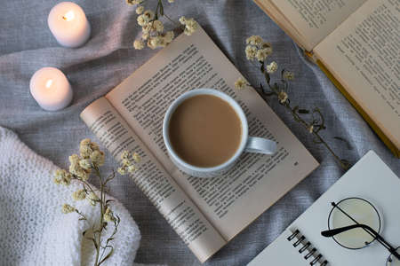Warm soft blanket, a cup of hot coffee, candles, flowers and open books on a gray background. Cozy still life. Flat Lay, Top View, Life Blog Concept.のeditorial素材