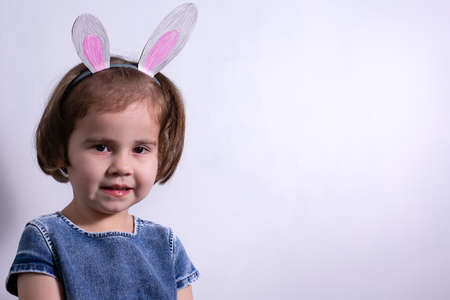 Happy Easter. A girl of three years old in bunny ears on her head on a white studio background....