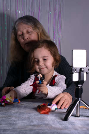 An elderly woman and a child are filming a video blog. Grandmother and granddaughter with a phone record video messages at home. Rest, relaxation, leisure concept.の写真素材