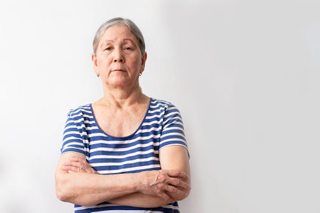 A woman in a striped blue and white dress has her arms crossed on a white background. Elderly senior...