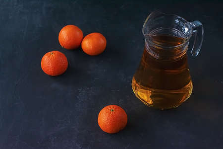 Jug with orange, tangerine juice and fruits on dark background