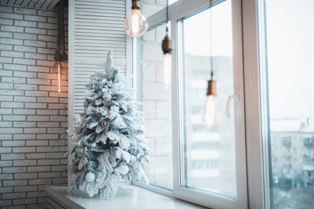 On the plastic windowsill is an artificial Christmas tree with snow.