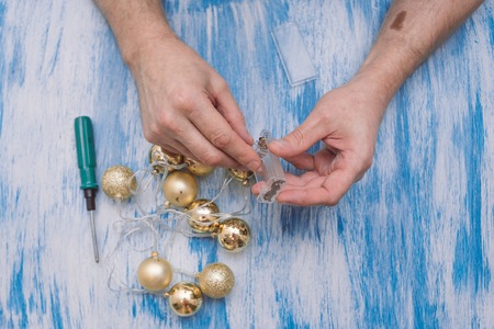 On a turquoise table a man with a screwdriver repairs a garland of gold balls.の写真素材