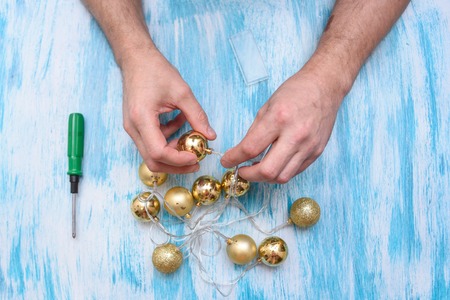 On a turquoise table a man with a screwdriver repairs a garland of gold balls.