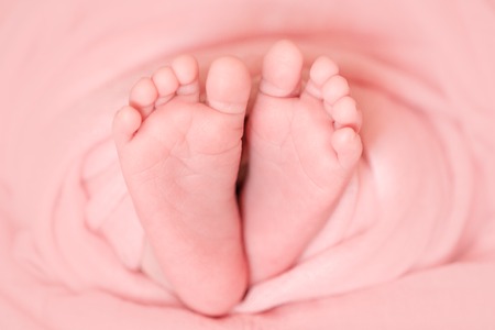 tender newborn baby feet with tiny toes wrapped in pink diaper, macroの写真素材