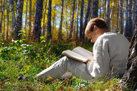 reading boy sit in autumn forest with a bookの写真素材