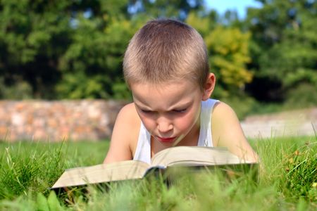 The child attentively reads the book on a summer meadowの写真素材