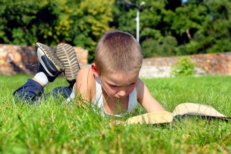 The child attentively reads the book on a summer meadowの写真素材