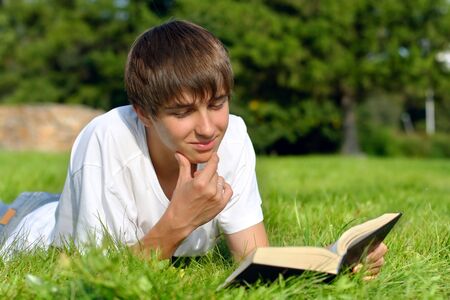 The teenager reads the book on a summer meadowの写真素材