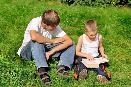 The happy teenager and kid with a book on a summer meadowの写真素材