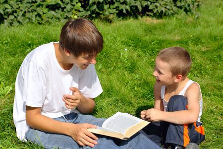 The happy teenager and kid with a book on a summer meadowの写真素材