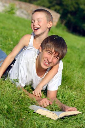 The happy teenager and kid with a book on a summer meadowの写真素材