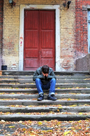 sad young man with hidden face on the old house backgroundの写真素材