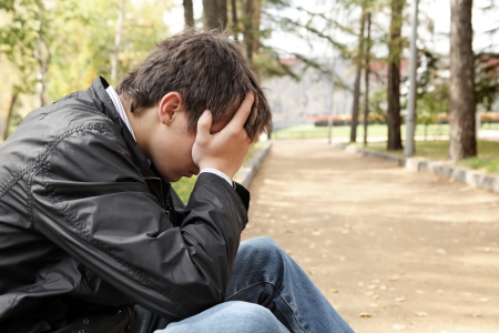 sad young man sitting in the autumn parkの写真素材